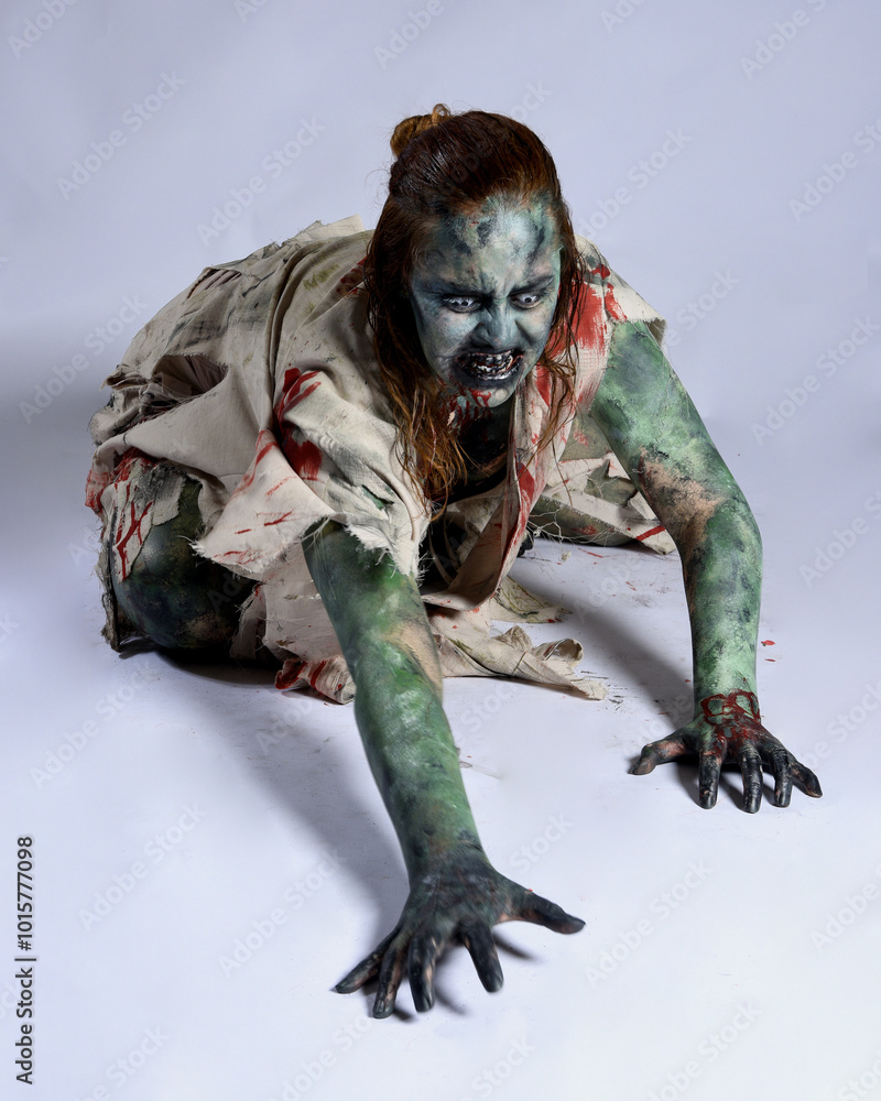 portrait of scary female model wearing spooky halloween costume, ripped clothes and fake blood like an undead demon apocalyptic zombie character. Isolated figure, crawling poses dark studio background portrait of scary female model wearing spooky halloween costume, ripped clothes and fake blood like an undead demon apocalyptic zombie character. Isolated figure, crawling poses dark studio background