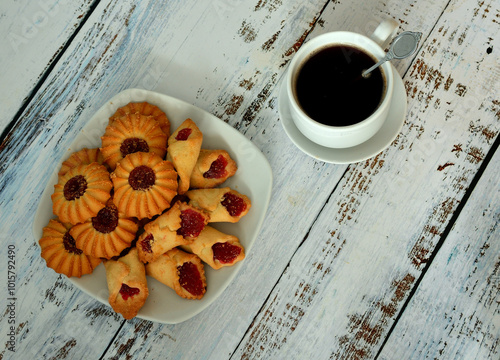 Kurabye, shortbread cookies with thick jam on a white plate and a cup of black coffee on a light wooden table. photo