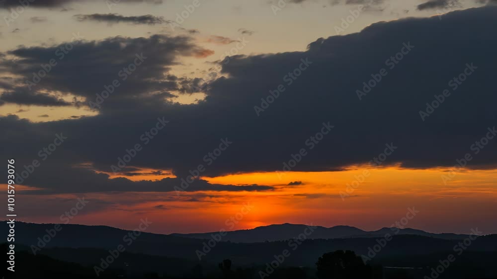 A stunning sunset with vibrant colors and rays illuminating the clouds over rolling hills.