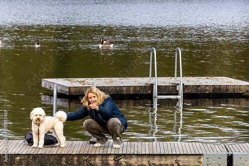 Photography Stockholm, Sweden A woman stands on a small lake pier with a Bichon Poo dog on an autumn day