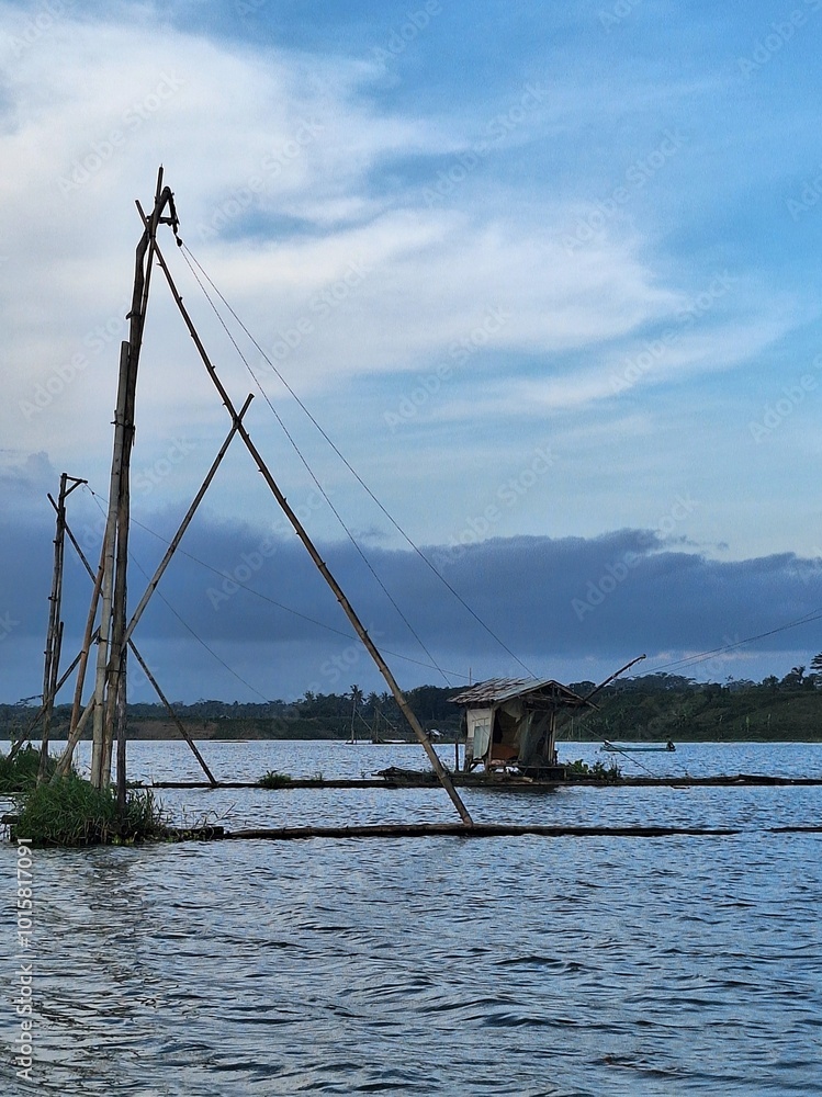 Fototapeta premium Traditional fish cages and a hut in the middle of a lake surrounded by hills, under the sunset sky, in Malang, Indonesia