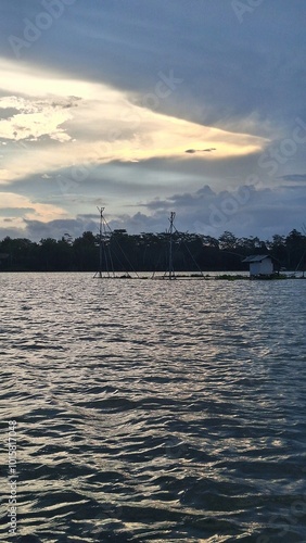 Traditional fish cages and a hut in the middle of a lake surrounded by hills, under the sunset sky, in Malang, Indonesia photo