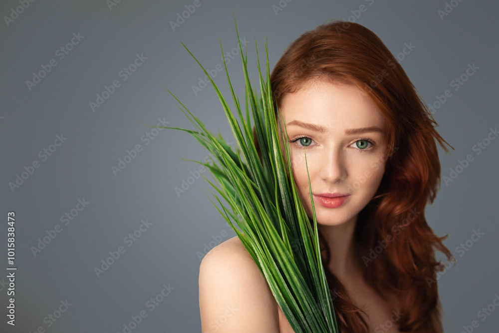 Pretty Ginger-Haired Girl Posing With Green Plant Leaves Standing Looking At Camera Over Gray Studio Background. Natural Beauty, Spa And Skincare Cosmetics Concept Pretty Ginger-Haired Girl Posing With Green Plant Leaves Standing Looking At Camera Over Gray Studio Background. Natural Beauty, Spa And Skincare Cosmetics Concept