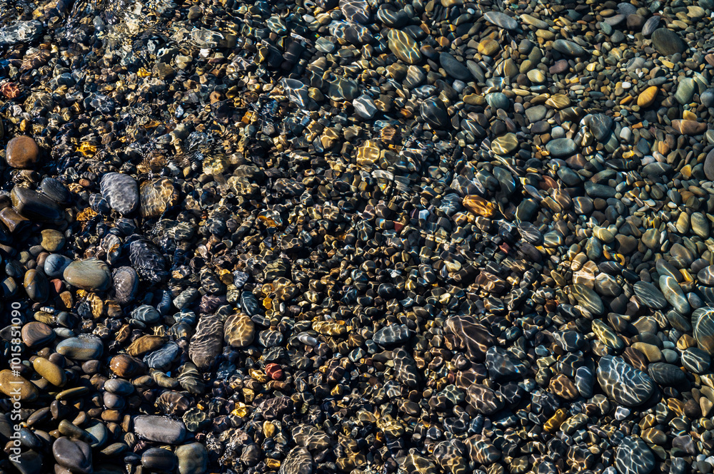 Underwater pebble backgrounds. Colorful stones sea bottom and sea fish in the sun rays. View from above through clear water. Seascape wallpaper texture. Underwater pebble backgrounds. Colorful stones sea bottom and sea fish in the sun rays. View from above through clear water. Seascape wallpaper texture.