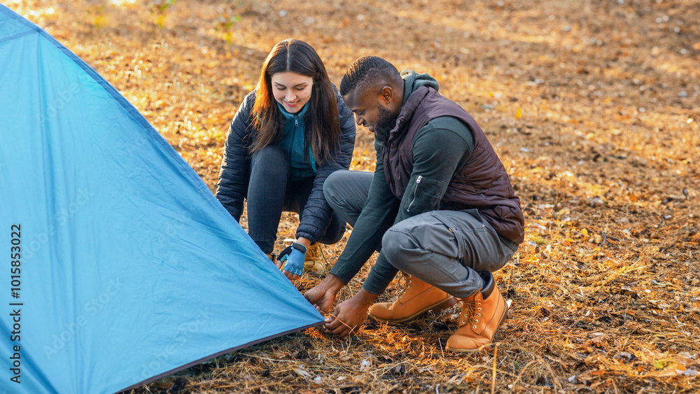 © Prostock-studio - Multiracial young couple setting tent, camping together in autumn forest © Prostock-studio - Multiracial young couple setting tent, camping together in autumn forest