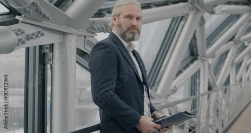 Wallpaper Mural Slow motion portrait of middle-aged businessman in elegant suit standing in modern glass hall holding folder with papers looking at camera. Business and finance concept. Torontodigital.ca