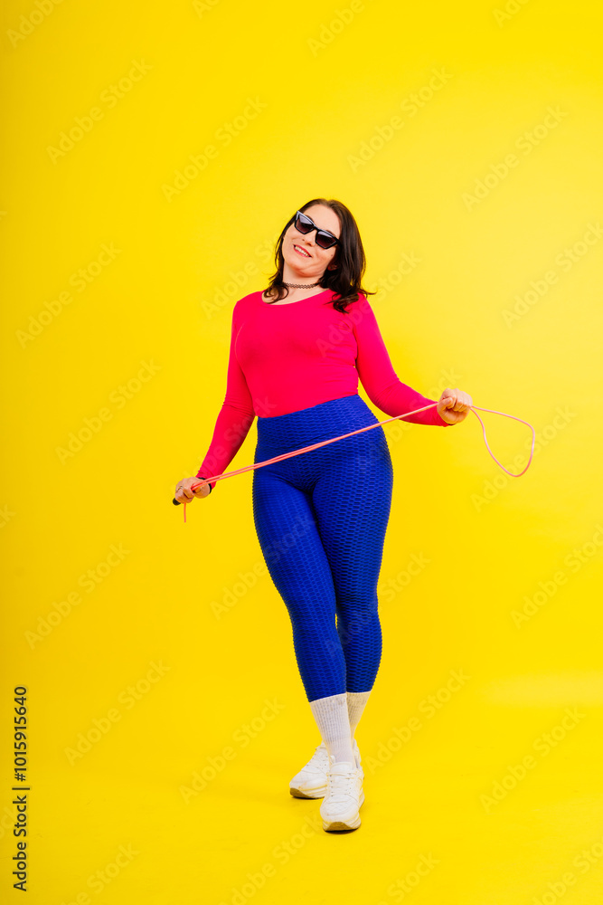 Pretty smiling plump female in sporty top and leggings holding jumping rope in hands Pretty smiling plump female in sporty top and leggings holding jumping rope in hands