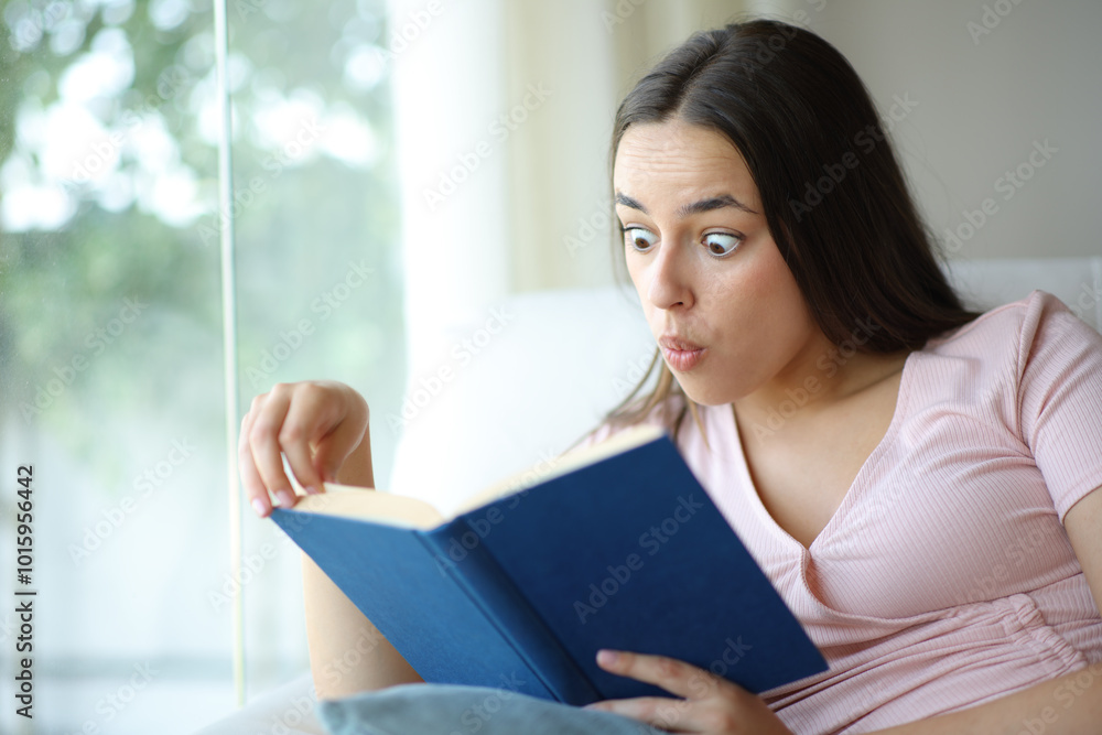 Amazed woman reading a paper book sitting in a sofa Amazed woman reading a paper book sitting in a sofa