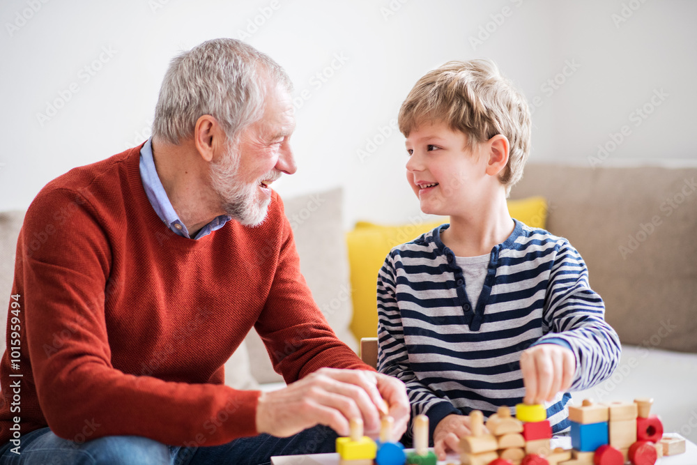 Naklejka premium Grandfather spending time with grandson, taking care of him while parents are at work. Boy and grandpa playing with wooden train.
