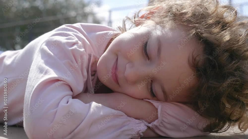 A 4-year-old girl with curly hair rests lying on the ground in her backyard, enjoying a peaceful and relaxing moment outdoors. A 4-year-old girl with curly hair rests lying on the ground in her backyard, enjoying a peaceful and relaxing moment outdoors.