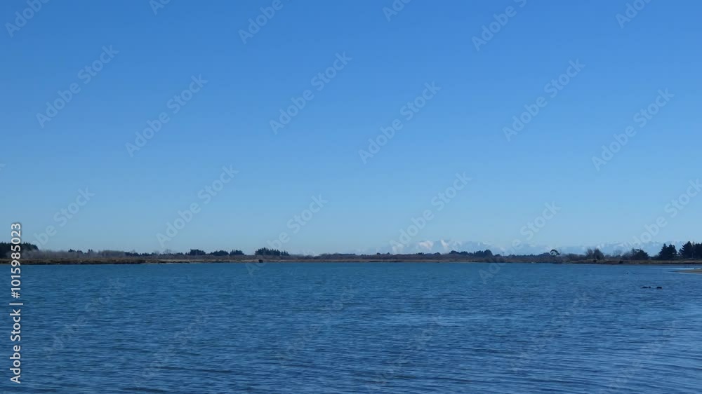 Incoming tide from ocean flows upstream on a beautiful winter's day before snow-capped foothills (Waimakariri River, New Zealand) Incoming tide from ocean flows upstream on a beautiful winter's day before snow-capped foothills (Waimakariri River, New Zealand)