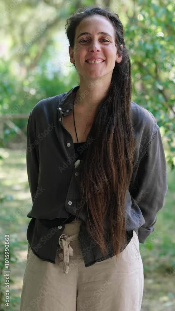 Vertical. A young woman with long hair smiles brightly while at a park, expressing happiness and contentment in a serene outdoor setting. Vertical. A young woman with long hair smiles brightly while at a park, expressing happiness and contentment in a serene outdoor setting.