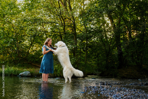 Young woman and her large white Great Pyrenees dog enjoying time together, cooling off in a stream during hot summer day. Pet owner, pet love, dog frienship concept. photo