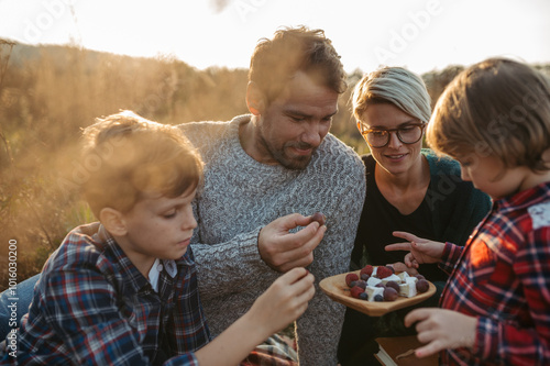 Portrait of family with two kids having picnic in autumn nature, eating fruits and cheese. photo