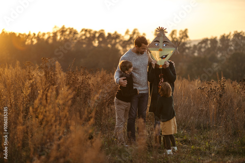 Portrait of young family flying a kite in the autumn nature, jumping in the middle meadow during sunset. Indian summer.