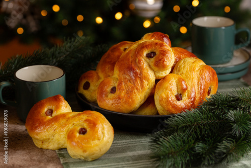 Christmas festive table with homemade swedish St Lucia saffron buns.  Coffe or tea cups. lussekatt or lussebulle, Cornish tea treat bun or revel bun, sweet bun flavoured with saffron and raisins. 