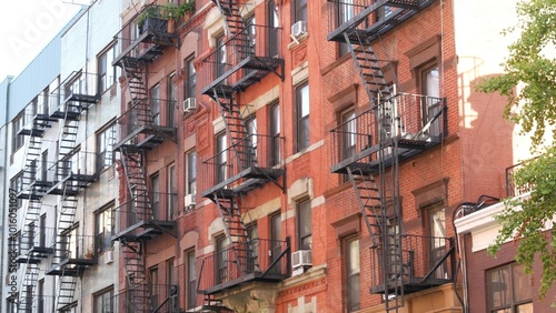 New York City classic building architecture, Manhattan, USA. Urban residential house exterior. Real estate property in United States. Typical red brick facade. Fire escape, emergency ladder exit.