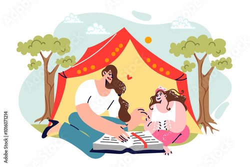 Family camping on summer vacation with mother reading book to daughter, sitting near tent in parks