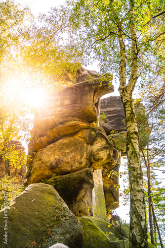 Golden sunlight filters through the vibrant autumn foliage, illuminating the majestic Besedice Rocks in Bohemian Paradise, creating a serene atmosphere for nature lovers. photo