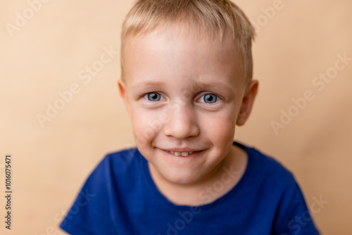 A cheerful young boy with bright blue eyes smiling against a light background in a cozy indoor setting captured during the afternoon