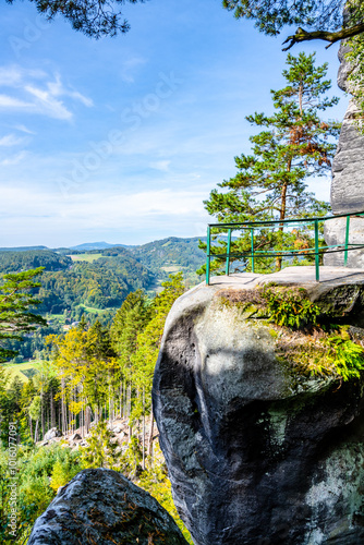 Visitors enjoy breathtaking autumn views from the Besedice Rocks in the Bohemian Paradise region of Czechia, surrounded by vibrant foliage and rugged terrain under a clear blue sky. photo