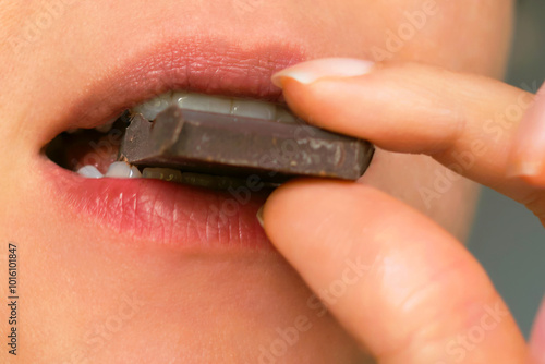 close-up of a person biting into a piece of dark chocolate, highlighting the rich flavor and indulgence of the treat. This image conveys a moment of sensory pleasure, perfect for gourmet, snack, or photo