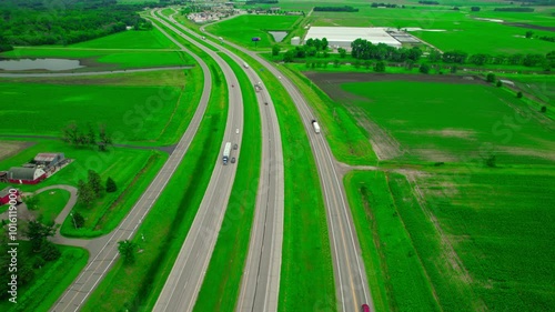 Orbiting aerial of Interstate 94 cutting through vibrant green farmlands in Minnesota, freight trucks with rural landscape. photo