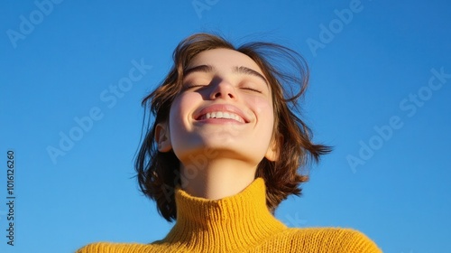 A young woman smiling with her eyes closed, head tilted back in genuine joy, under a clear blue sky