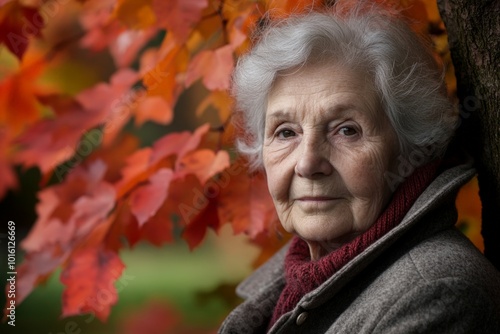 An elderly woman leans against a tree adorned with vivid autumn leaves, presenting a portrait rich in natural color and contemplative expression amidst the fall scenery.