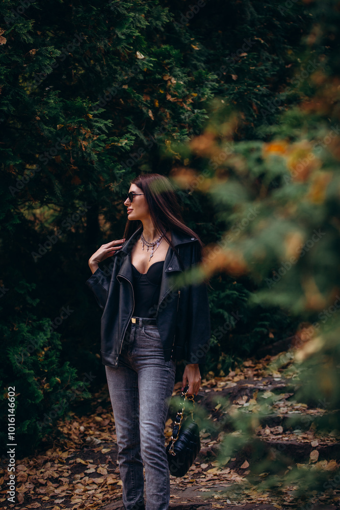 Woman, an adult and a beautiful brunette in a leather jacket and jeans, walks in the park in autumn. Woman, an adult and a beautiful brunette in a leather jacket and jeans, walks in the park in autumn.