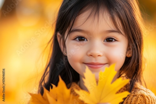 A girl with a pure and happy smile holds a yellow leaf, basking in golden sunlight, showcasing the joy and wonder of a crisp and colorful autumn day.