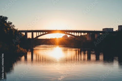 A peaceful sunset casts warm hues over the river, highlighting the silhouette of a bridge. The reflection in the water enhances the tranquil scene beautifully.