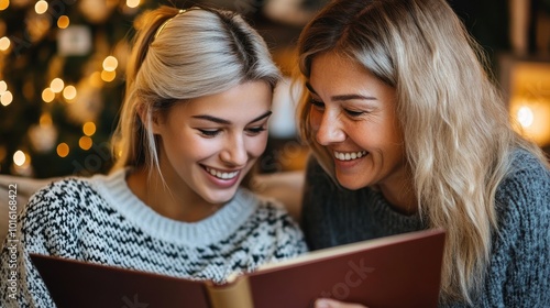 Two women are smiling as they share a joyful moment reading a book together during the holidays