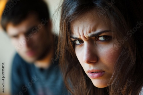 A tense woman in focus confronts a dim, blurry male figure in the background, capturing a moment of confrontation and tension amidst a personally charged scene. photo