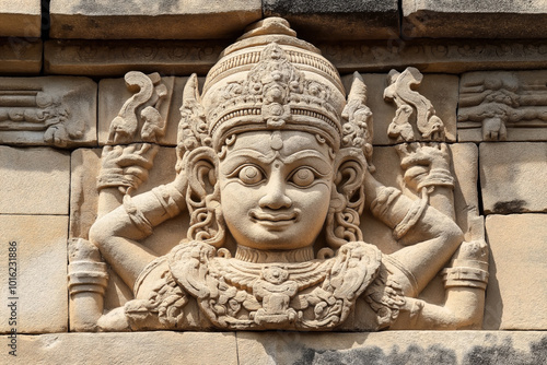 Intricate stone carving of a deity with multiple arms, adorned with ornate headgear and jewelry, on an ancient architectural structure.