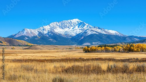 Snow-capped peaks rise majestically over a vibrant autumn landscape with golden grasses in the foreground, showcasing nature's breathtaking seasonal transition.