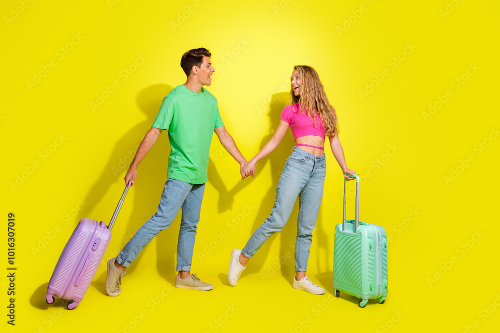 Full size photo of two nice young people hold arms suitcase isolated on bright yellow color background Full size photo of two nice young people hold arms suitcase isolated on bright yellow color background