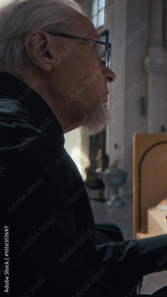 Vertical view of skilful grey-haired senior musician in black shirt playing electric organ in temple Vertical view of skilful grey-haired senior musician in black shirt playing electric organ in temple