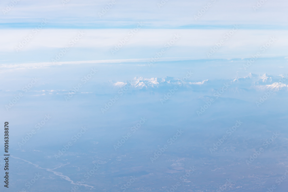 Fototapeta premium Aerial view of snowy mountain tops covered in clouds. Majestic blue mountains view from above