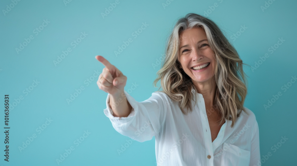 Smiling woman with long wavy hair points to the right against a light blue background in a casual setting Smiling woman with long wavy hair points to the right against a light blue background in a casual setting