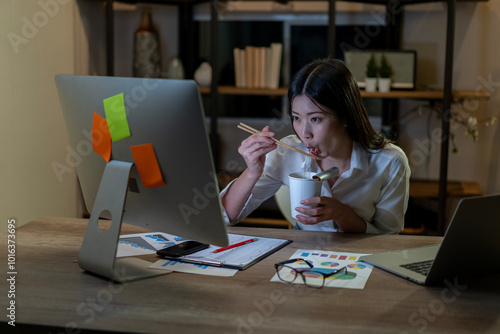 Young businesswoman working at night in office eating instant noodles