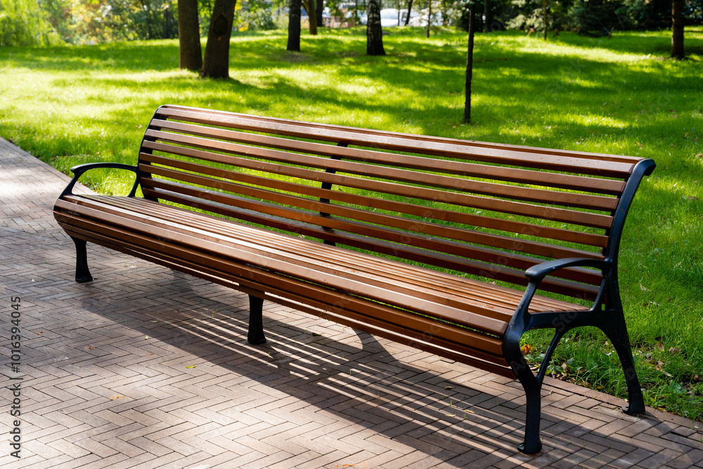 A long, sturdy wooden bench is situated in a beautiful park, surrounded by lush green trees in the background, creating a peaceful outdoor setting for relaxation and enjoyment A long, sturdy wooden bench is situated in a beautiful park, surrounded by lush green trees in the background, creating a peaceful outdoor setting for relaxation and enjoyment