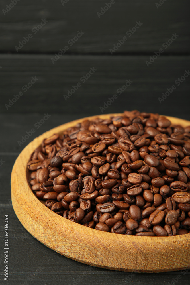 Fototapeta premium Coffee beans on wooden plate on black wooden background. Vertical photo