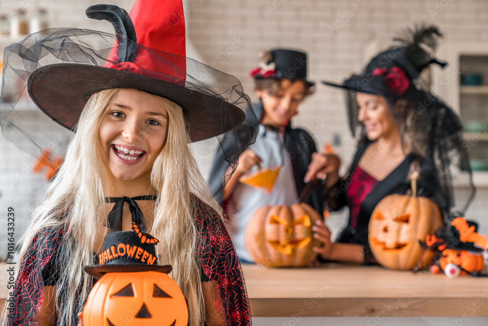Fototapeta premium Portrait of smiling girl with pumpkin. Happy family preparing for Halloween. Woman and children wearing costumes celebrating posing with carved pumpkins looking at camera. Celebration concept