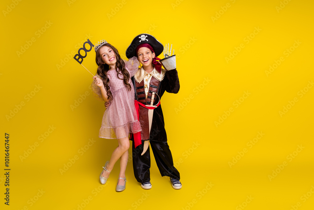 Full size photo of small two kids halloween princess pirate costume boo arm wave hi isolated on yellow color background Full size photo of small two kids halloween princess pirate costume boo arm wave hi isolated on yellow color background