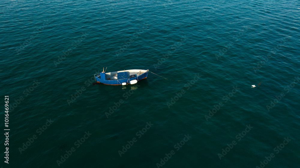 Aerial view of a one small fishing boat anchored in the middle of the sea. The boat is empty and lonely. Aerial view of a one small fishing boat anchored in the middle of the sea. The boat is empty and lonely.