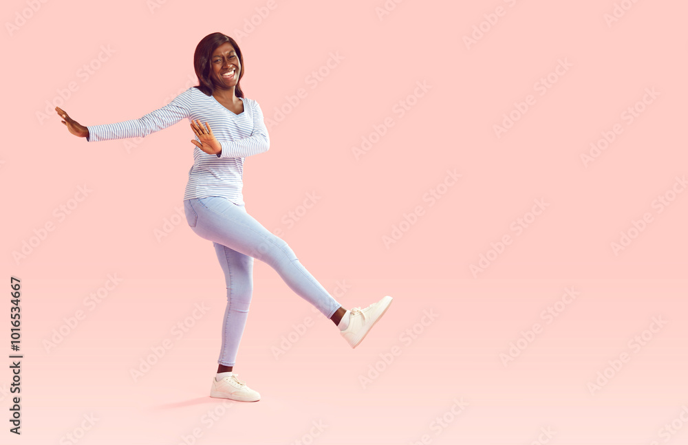 Cheerful positive young african american woman in good mood having fun on pink studio background. Full length dark-skinned girl in casual clothes steps and dances near copy space. Advertising banner. Cheerful positive young african american woman in good mood having fun on pink studio background. Full length dark-skinned girl in casual clothes steps and dances near copy space. Advertising banner.