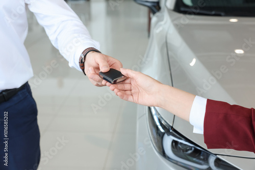 Salesman giving key to client near new car in salon, closeup