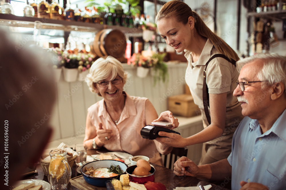 Senior woman paying with smartphone for meal with friends at restaurant Senior woman paying with smartphone for meal with friends at restaurant