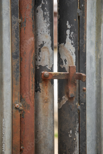 close-up of old rusty flip latch lock on metal outdoor gate, corroded locking hardware in soft focus and copy space